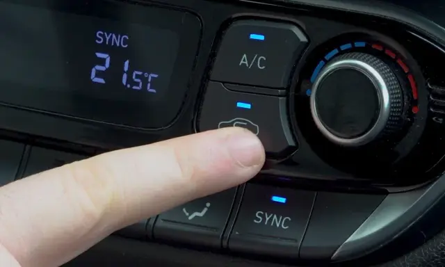 Dedo presionando el botón recirculacion aire del climatizador del coche.