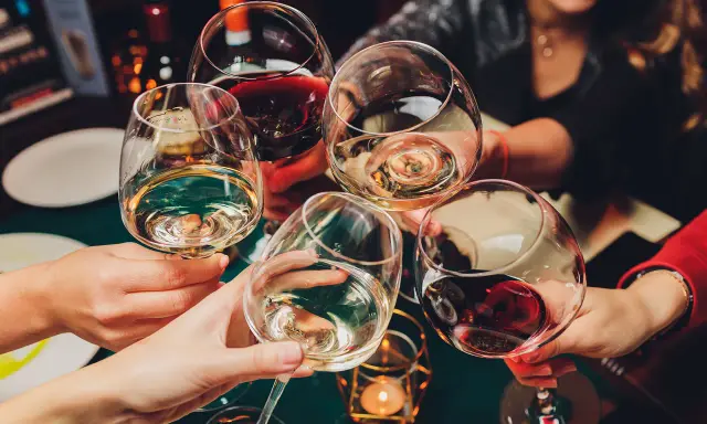 Hände heben Gläser mit Weiß- und Rotwein zum Anstoßen. Die ideale trinktemperatur für den Wein wird genossen.