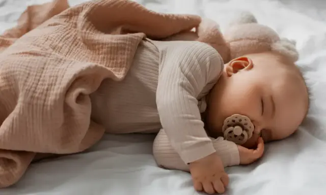 Spokojny sen niemowlaka na boku, z otulającym kocykiem. Pozycja ta jest dobra dla bioderek.