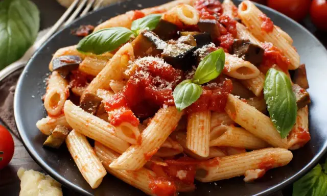 Un plato de pasta alla norma con penne, berenjena, salsa de tomate y albahaca fresca, espolvoreado con queso rallado.
