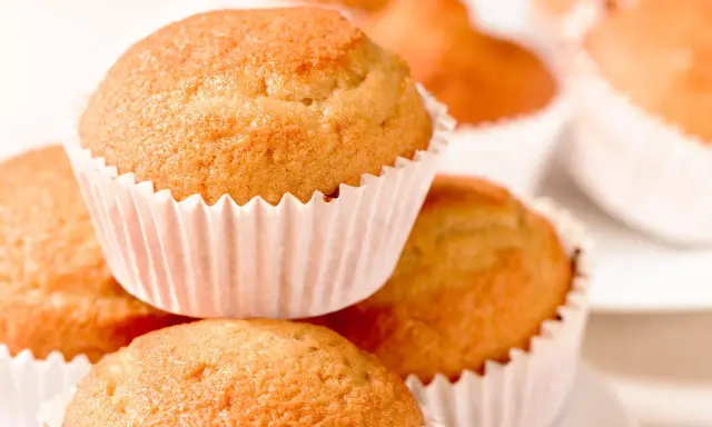 Ein Stapel goldbrauner, veganer Muffins in weißen Papierförmchen. Sie sehen köstlich und frisch gebacken aus.