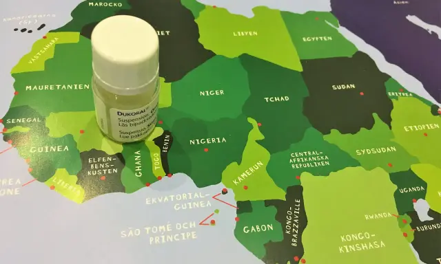 En liten flaska Dukoral® står på en karta över Afrika, nära Guinea och Elfenbenskusten.