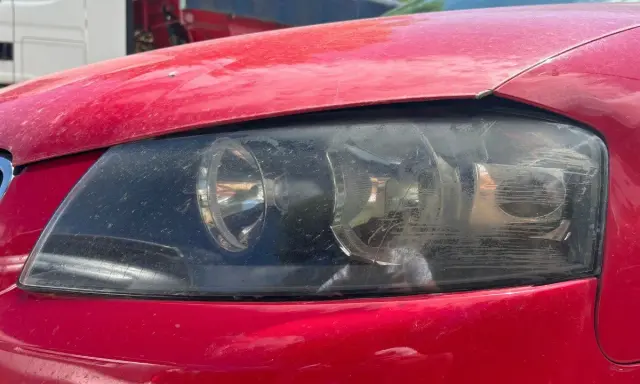 Faros sucios de coche rojo. El faro izquierdo muestra un anillo de luz, el derecho está rayado. La luz marcha atrás obligatoria es esencial para la seguridad.