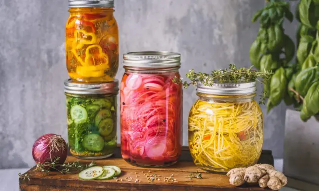 Bunte Gläser mit eingelegtem Gemüse, perfekt für ein mixed pickles rezept. Gurken, rote Zwiebeln und gelbe Paprika sind sichtbar.