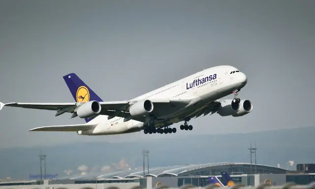 Samolot pasażerski Lufthansa z wysuniętym podwoziem startuje na tle lotniska.