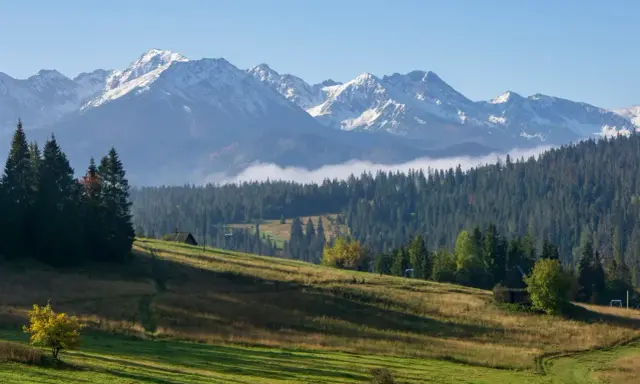 Widok na Tatry z Gubałówki. W oddali ośnieżone szczyty, niżej las i zielone zbocza. Widać fragment kolejki.