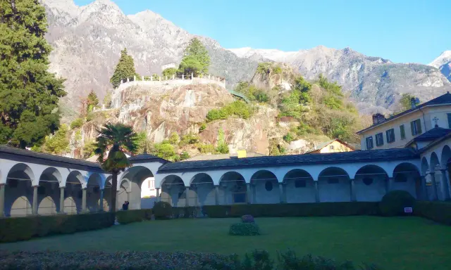 Un porticato ad archi domina un giardino curato, con montagne imponenti sullo sfondo. Un luogo ideale per scoprire cosa vedere a Chiavenna.