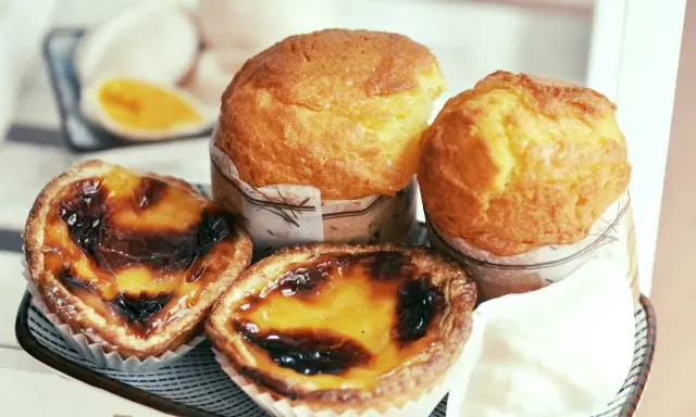Pyszne portugalskie ciastka, w tym dwa kremowe pastel de nata i dwa muffinki, kuszą apetycznym wyglądem.