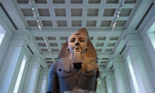 A colossal bust of an ancient Egyptian pharaoh, one of the museum's famous sculptures, stands majestically under a grand, coffered ceiling.