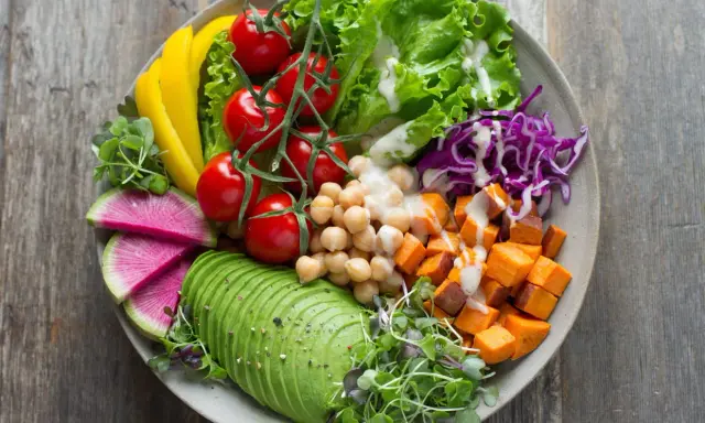 Une salade de crudités colorée et nutritive : avocat, tomates, pois chiches, patates douces, chou rouge, poivron jaune et pousses fraîches.