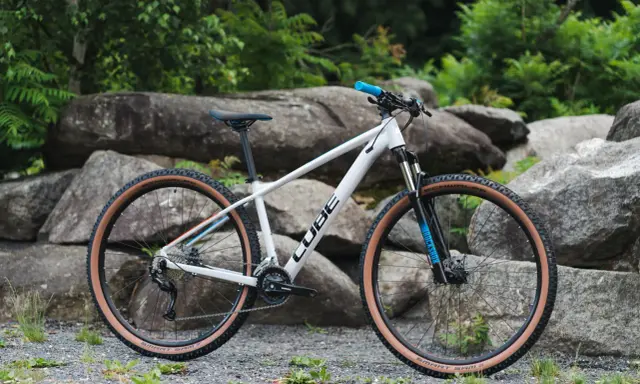 Biały rower Cube z brązowymi oponami, idealny jako rower na długie trasy. Wyposażony w amortyzator RockShox i napęd Shimano.