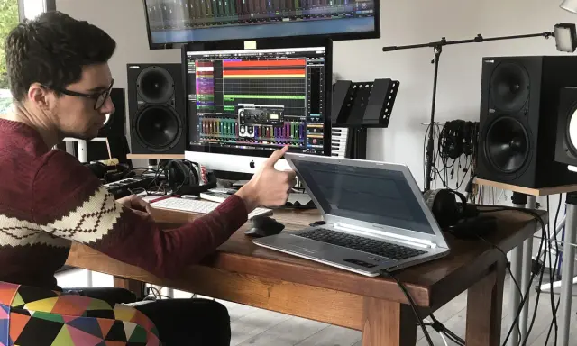 Un jeune sound engineer travaille dans son studio, entouré de matériel audio, d'écrans et d'un clavier.