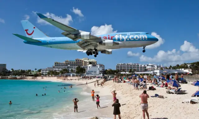 Samolot Airfly.com przelatuje nisko nad plażą pełną turystów, którzy obserwują jego lądowanie.