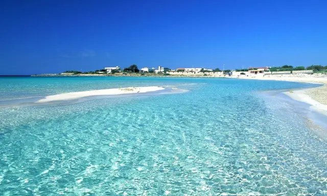Acque cristalline lambiscono spiagge bianche, con un villaggio sullo sfondo sotto un cielo azzurro intenso.