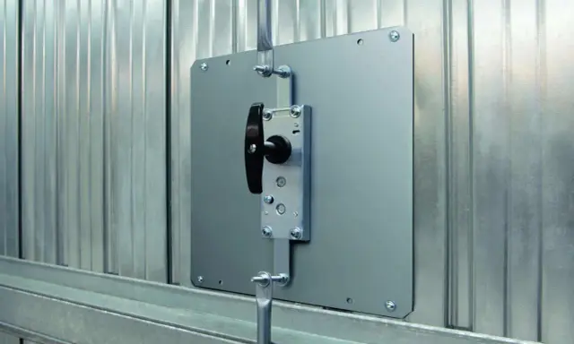 Système de verrouillage pour securiser porte garage. Poignée noire sur plaque métallique fixée sur porte en métal ondulé.