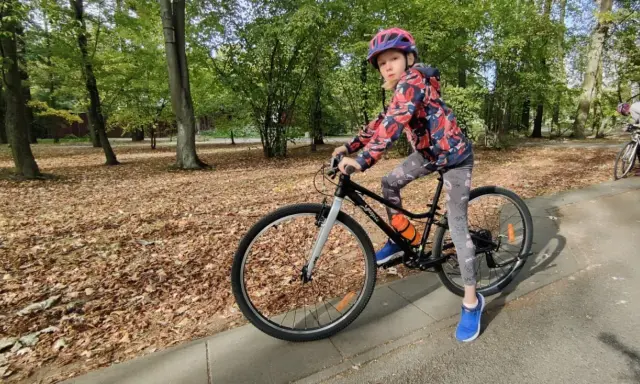 Dziewczynka na rowerze, idealny rozmiar roweru dla 10 latka. Jesienny park, liście na ziemi.