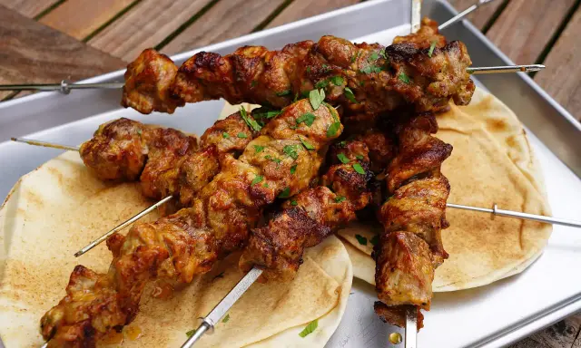 Saftige Schaschlik-Spieße, perfekt gegrillt, liegen auf Fladenbrot. Ein Genuss, der an ein gemütliches Essen im Dutch Oven erinnert.