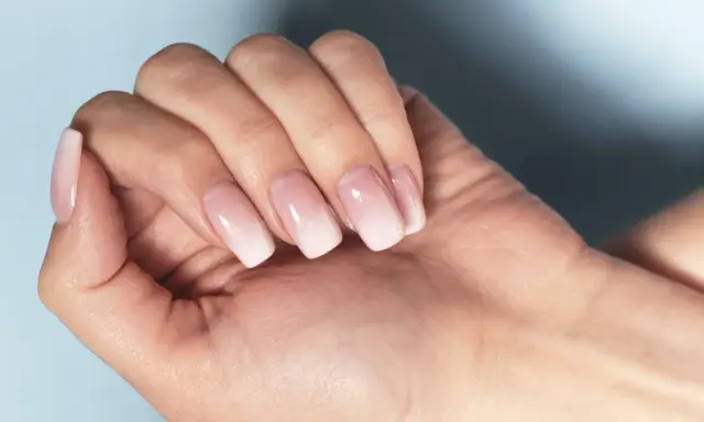 Dłoń z paznokciami w stylu francuski manicure, z delikatnym ombre od różu do bieli.