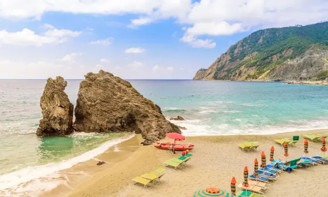 Spiagge sabbia Liguria: scogli imponenti, mare turchese e lettini pronti per il relax.