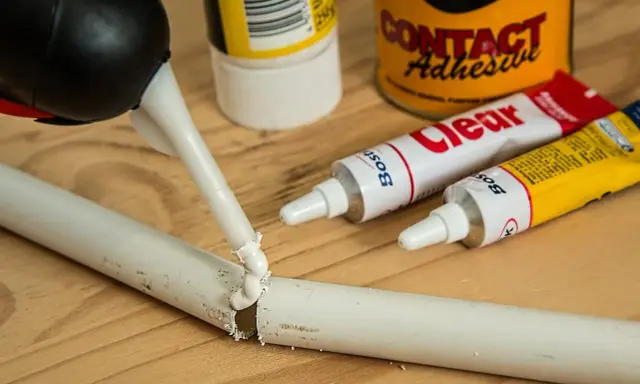 Klej w pistolecie aplikowany na białą rurkę. Obok tubki z klejem i puszka "Contact Adhesive". Jak usunąć klej po naklejce z metalu?