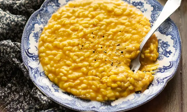 Un cremoso risotto alla zucca, servito su un piatto decorato, con una forchetta che affonda nel piatto.