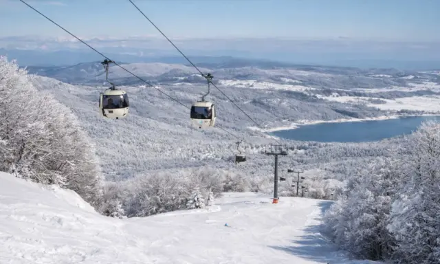 Funivia su montagne innevate, un lago azzurro sullo sfondo. Scopri dove sciare in Calabria per un'esperienza indimenticabile.