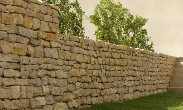 Un muret en pierre sèche, bordé d'herbe verte et de verdure luxuriante, s'étend sur la droite, menant à des marches en pierre.