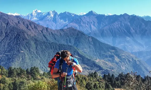 Mężczyzna z plecakiem i kijkami podczas trekkingu w Himalajach, podziwiający majestatyczne szczyty.