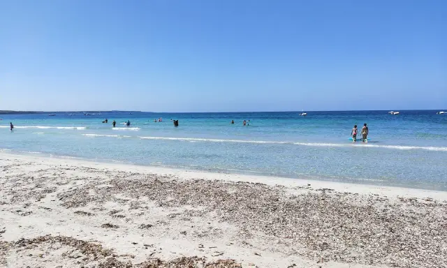 Spiaggia di Arbatax con sabbia chiara e mare cristallino, bagnanti e barche all'orizzonte. Un angolo di paradiso che ricorda la spiaggia rosa.