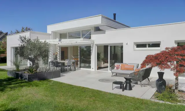 Une maison moderne avec une terrasse aménagée, un salon extérieur et un jardin. Ce projet d'extension de maison offre un espace de vie lumineux et agréable.