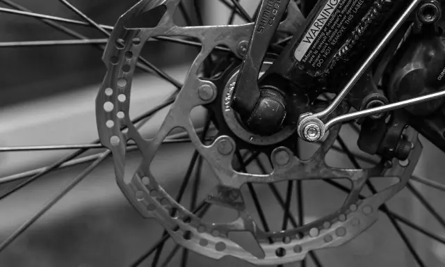 Zbliżenie na tarczę hamulcową i piastę roweru. Widoczne są szprychy, zacisk hamulcowy i dźwignia Shimano. To kluczowe elementy wpływające na przełożenia w rowerze.