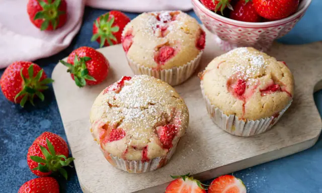 Saftige Erdbeer Muffins, bestäubt mit Puderzucker, liegen auf einem Holzbrett, umgeben von frischen Erdbeeren.