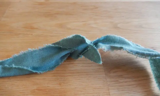 En bit tygremsa, redo att sy ihop trasmattor. Trådar hänger löst från kanterna.