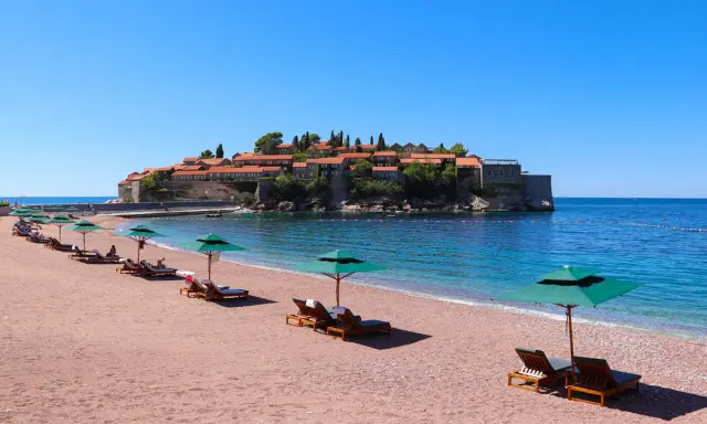 Ein idyllischer montenegro sandstrand mit Liegestühlen und Sonnenschirmen, im Hintergrund die malerische Insel Sveti Stefan.