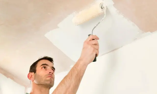 Hombre pintando el techo con rodillo. Se ve la mano sujetando el rodillo y la pintura blanca aplicándose.