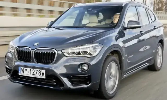 Ciemnoszary BMW X1 2025 z kierowcą za kierownicą, jadący po drodze.