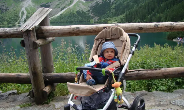 Niemowlak w wózku podziwia Tatry. Piękny widok na jezioro i góry.