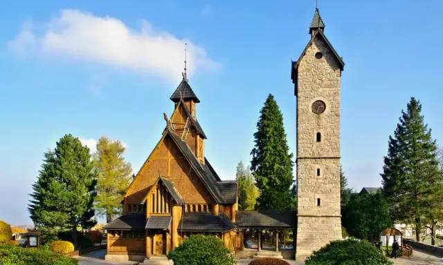 Drewniany kościółek i kamienna wieża z zegarem, jedne z głównych atrakcji Karpacz i okolice, na tle błękitnego nieba.