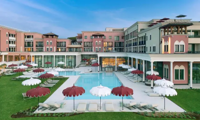 Un resort da sogno a Caorle, con piscina azzurra, lettini e ombrelloni rossi e bianchi. Un cavallino bianco potrebbe galoppare felice in questo paradiso.