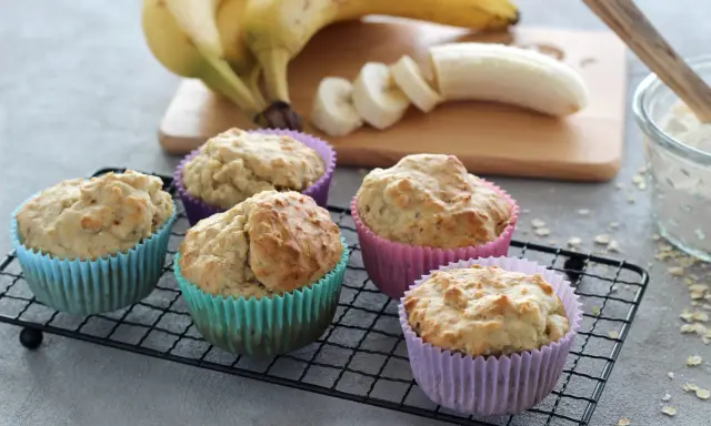 Fünf leckere bananenmuffins ohne zucker in bunten Förmchen auf einem Gitter. Bananen und Mehl im Hintergrund.
