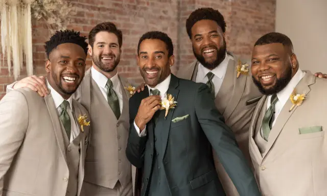 Groomsmen in light tan suits and one in a dark green suit, all smiling. They are dressed for a wedding, showing when grooms get suits.