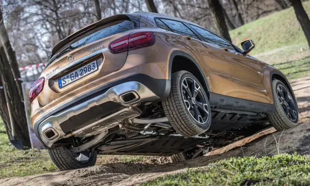 Złoty Mercedes GLA 220 4MATIC pokonuje nierówny teren, unosząc jedno koło.