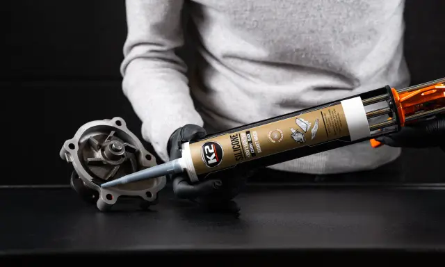 Ręce w czarnych rękawiczkach aplikują czarny silikon K2 na część pompy wodnej. Zastanawiasz się, ile schnie silikon? Ten produkt jest odporny na wysokie temperatury.