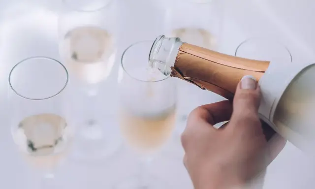 Eine Hand gießt Champagner in ein Glas. Die Bläschen steigen auf und lassen erahnen, wie gut der Champagner schmeckt.