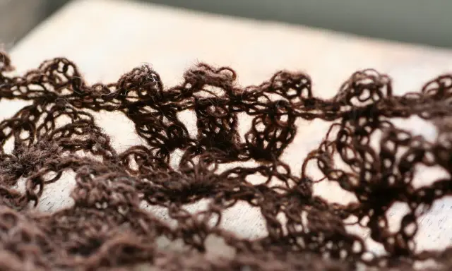 Close-up of a brown, lacy crocheted fabric with an openwork pattern.