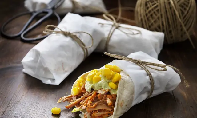 En läcker pulled pork wrap med majs och avokadokräm, inslagen i papper och bunden med snöre.
