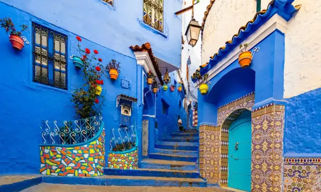 Maroko gdzie na wakacje? Urokliwa, niebieska uliczka w Chefchaouen z kolorowymi doniczkami i mozaikami zaprasza do odkrywania.