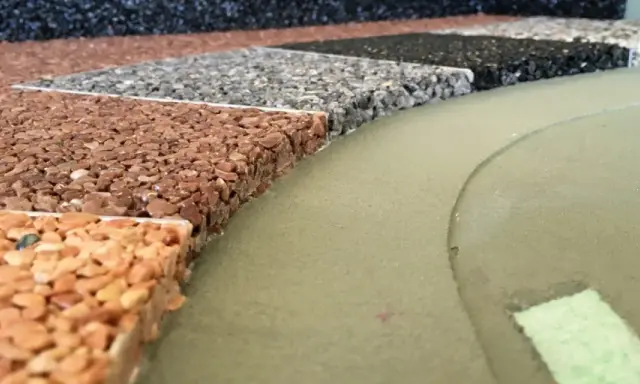 Przykładowe wykończenie tarasu betonowego: próbki nawierzchni z kamienia naturalnego w różnych kolorach, obok zielonej, gładkiej powierzchni.