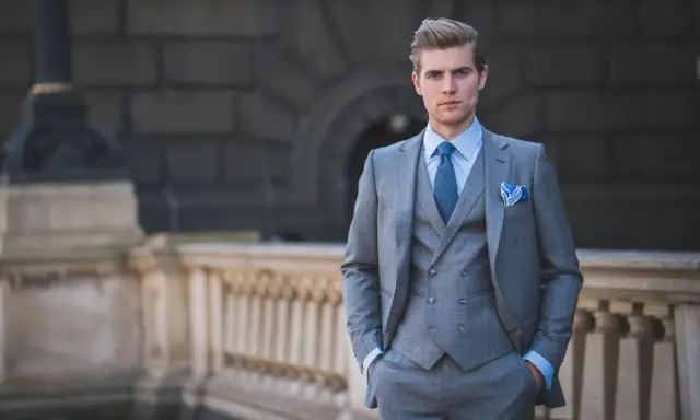 A man in a sharp grey suit, vest, and blue tie exemplifies formal cocktail attire for men, ready for any elegant event.