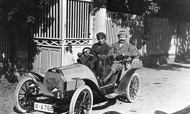 Zwei Männer in einem Bugatti, der aus Molsheim stammt, fahren durch eine sonnige Straße.